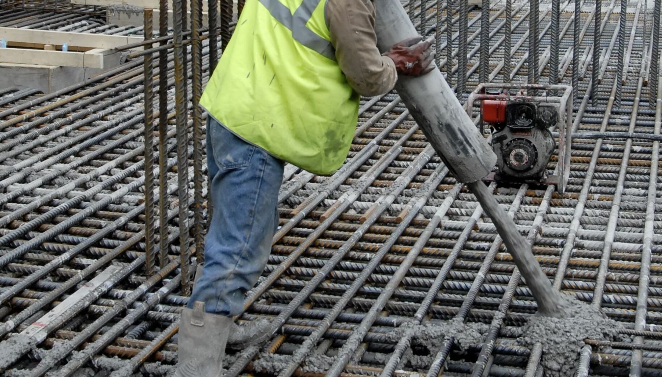 Construction worker in yellow vest vibrating concrete over a large rebar grid for a commercial foundation