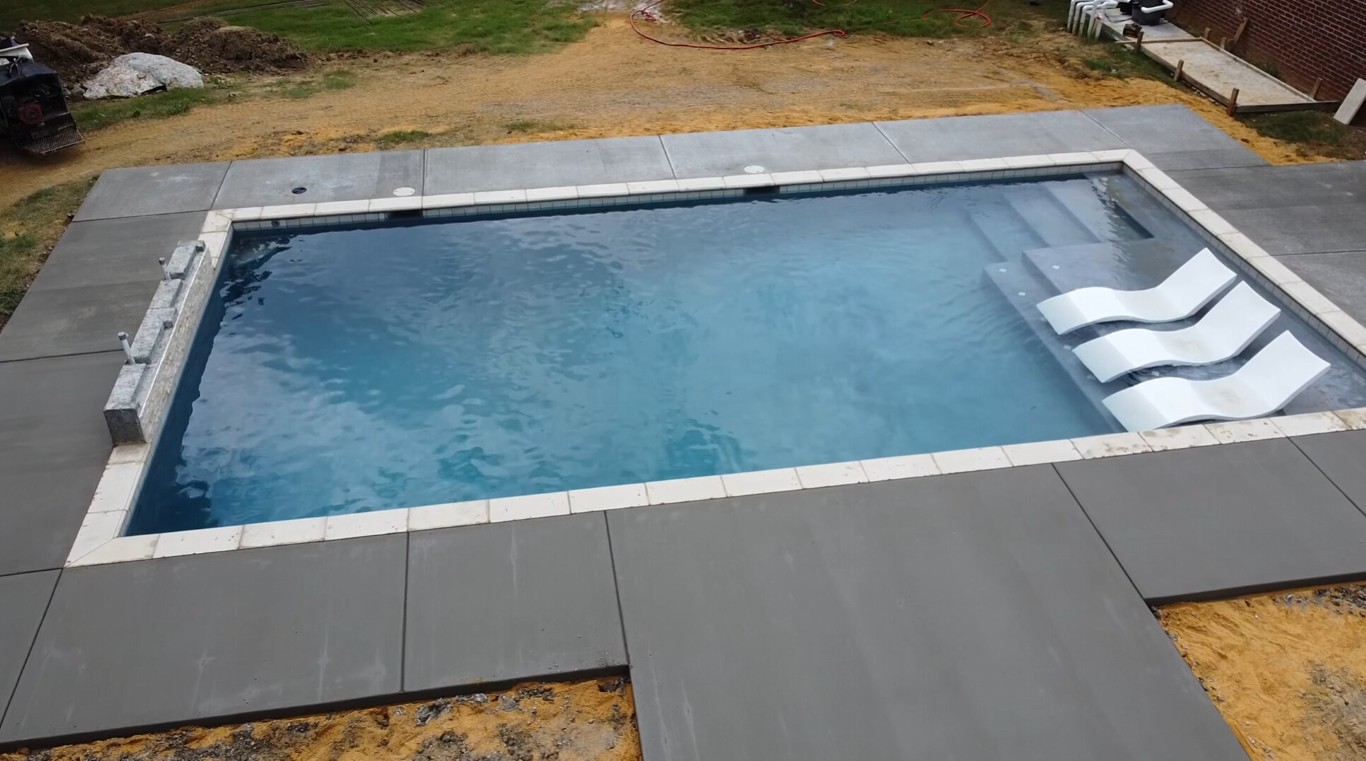 Newly installed smooth concrete pool deck surrounding an in-ground swimming pool
