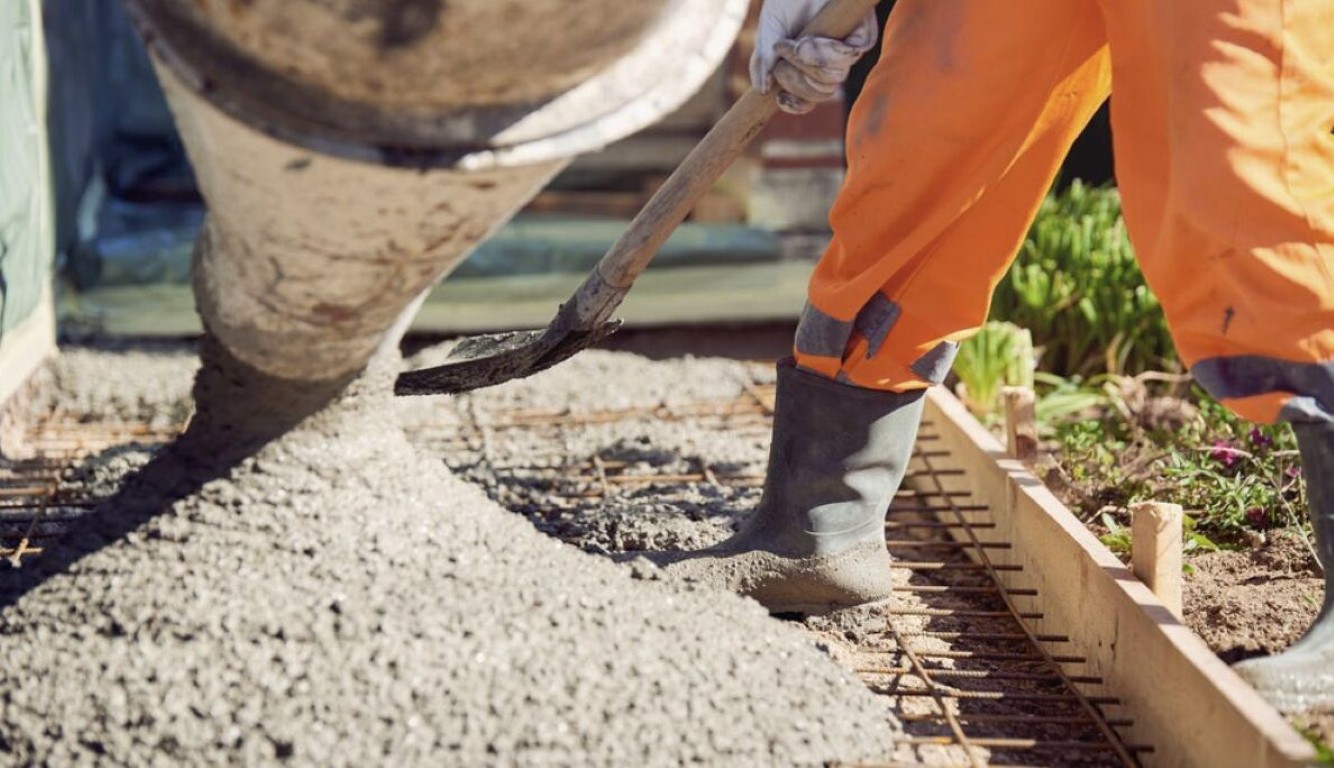 Concrete contractor in orange overalls spreading fresh concrete over reinforced rebar grid